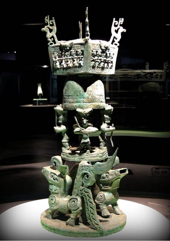 A sacrificial altar with several four-legged animals at the base to support a few bronze figures closely resembling the large face masks