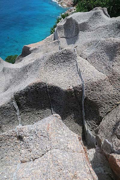 Ejemplo de roca granítica en el acantilado de Gros la Tête – Isla Aride, Seychelles.  Las capas delgadas más brillantes son vetas de cuarzo, formadas durante las últimas etapas de cristalización de magmas graníticos.  A veces también se les llama "venas hidrotermales".  (Etan J. Tal/CC BY SA 4.0)
