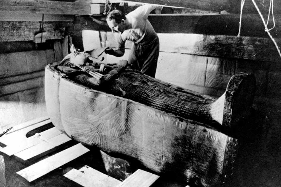 Говард Картер работает над крышкой второго (среднего) гроба, все еще находящегося в футляре первого (самого внешнего) гроба в погребальной камере Тутанхамона. (Всеобщее достояние)