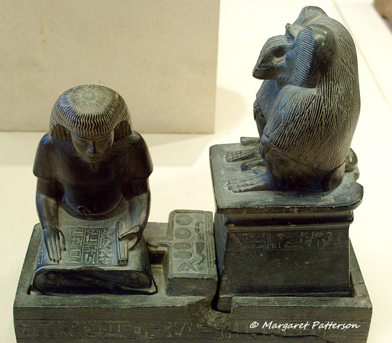 Scribe Nebmerutef is portrayed under the attentive gaze of the god Thoth, patron of writing. He is engrossed in reading a document, seated cross-legged on the ground, with his torso leaning slightly forward, and his right hand resting on the papyrus. Above him, the baboon sacred to Thoth is seated on a pedestal. New Kingdom. Louvre Museum, Paris.