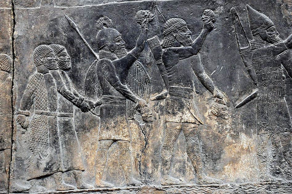 Assyrian soldiers carry beheaded heads of their prisoners as depicted on a wall in the South-West Palace at Nineveh, during the “First” Fall of Neneveh.          Source: Osama Shukir Muhammed Amin / CC BY-SA 4.0