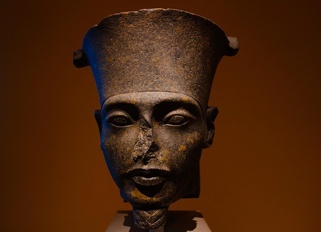 A striking close-up of a dark stone bust depicting Pharaoh Akhenaten