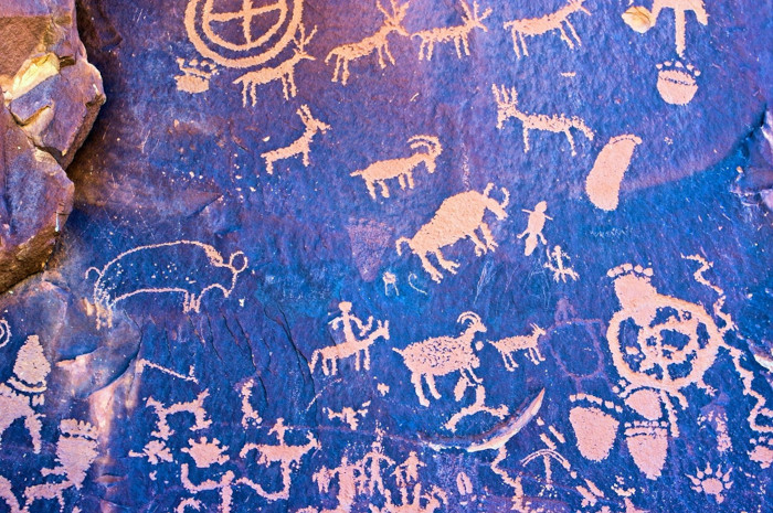 Blue-tinted ancient rock art showing human and animal figures. 