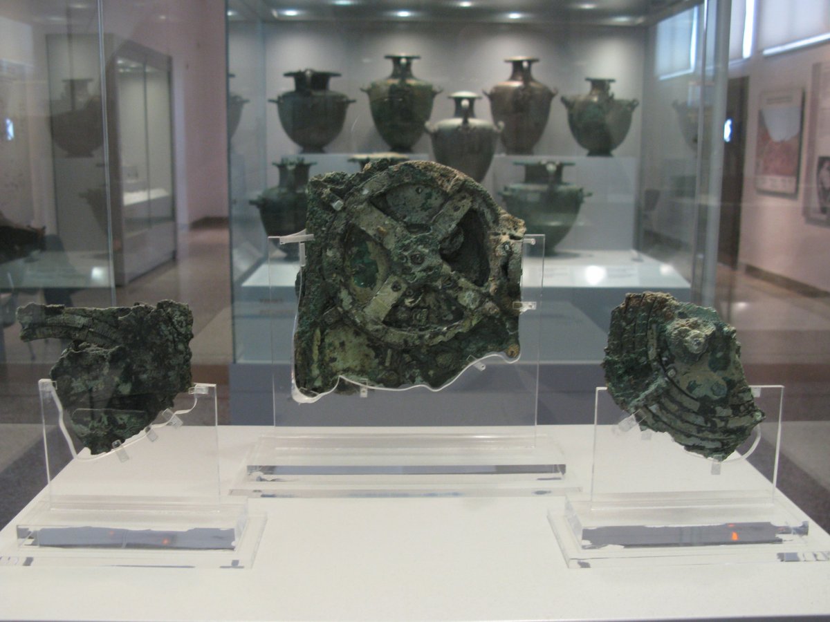 Three corroded bronze fragments on clear stands in a museum display case