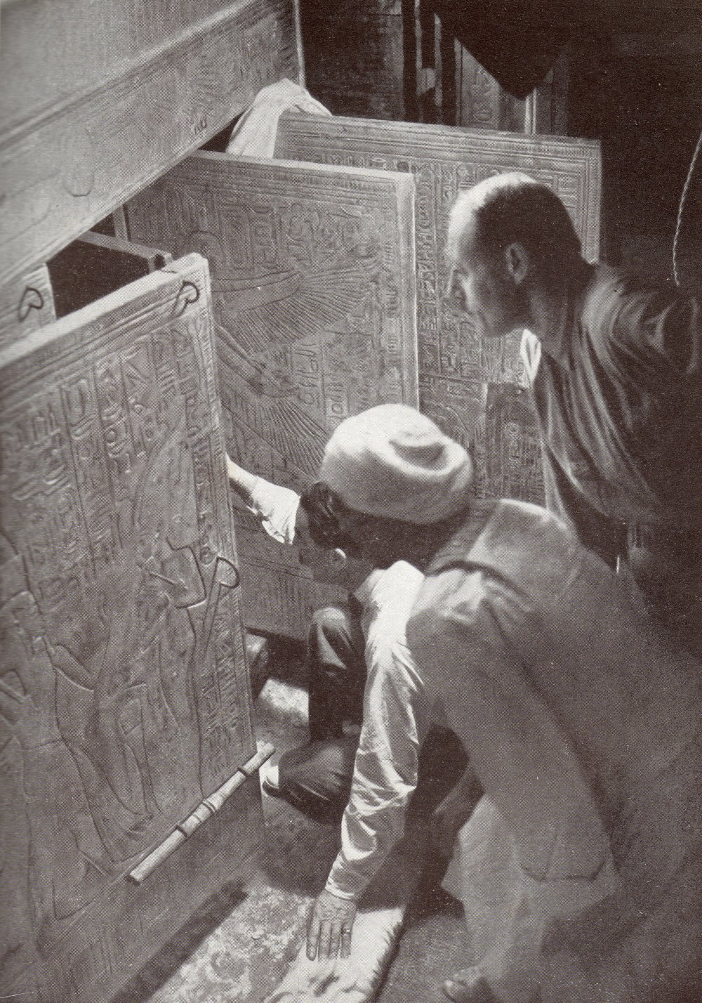 Black and white photo of Howard Carter and two men opening the doors of a gilded shrine carved with hieroglyphs