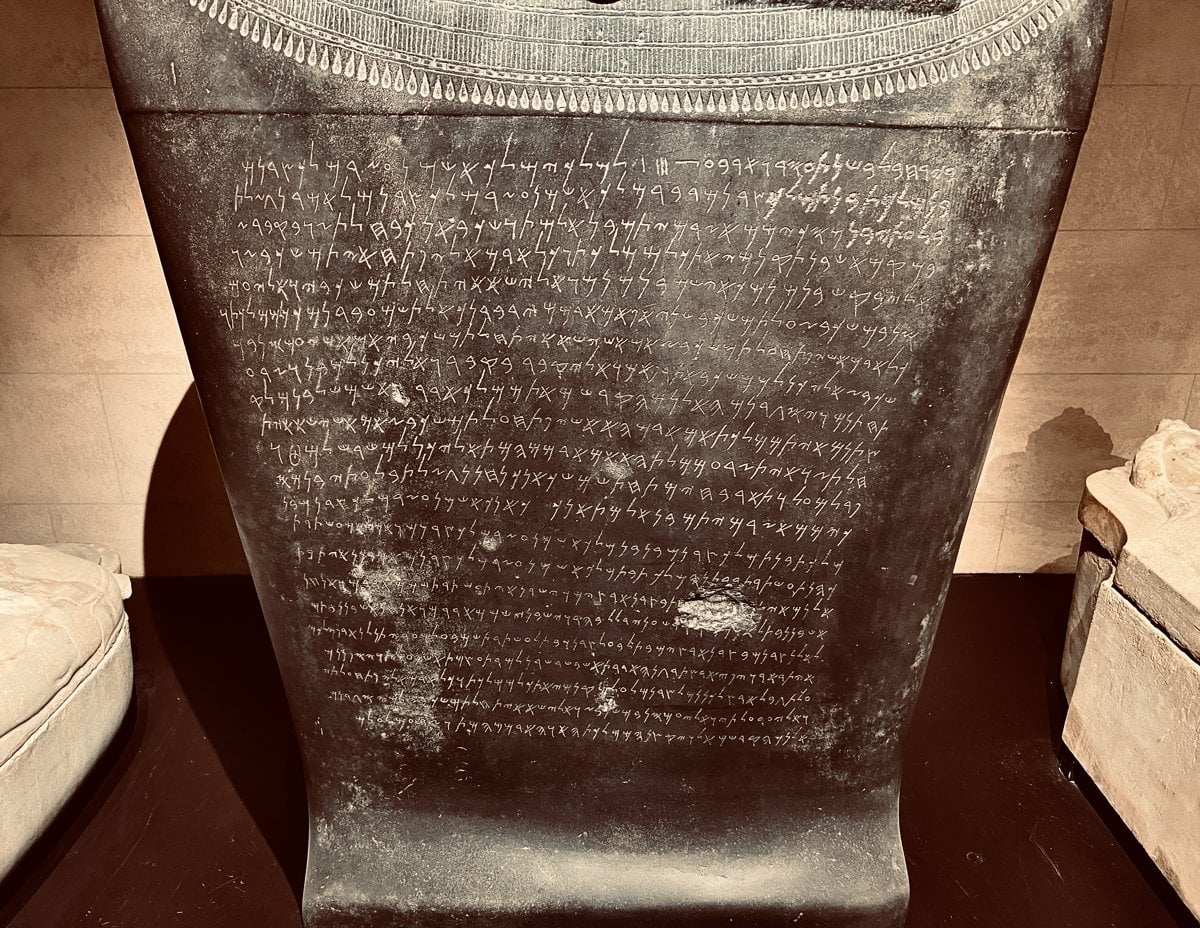 Rows of Phoenician letters carved across the dark stone of a sarcophagus in a museum case