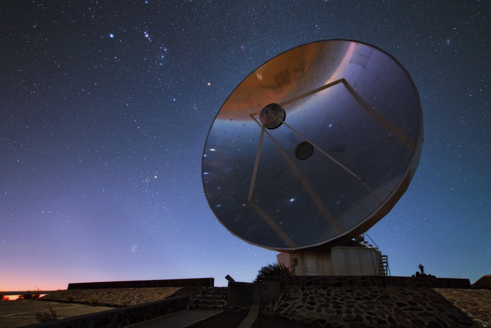 Night sky with the constellation Orion and its three belt stars above a dish telescope