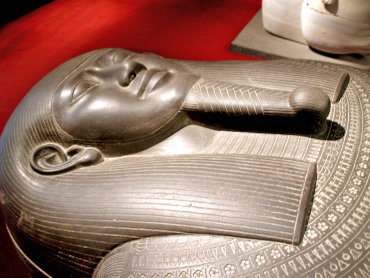 The black stone lid of an Egyptian style sarcophagus with a carved human face and wig