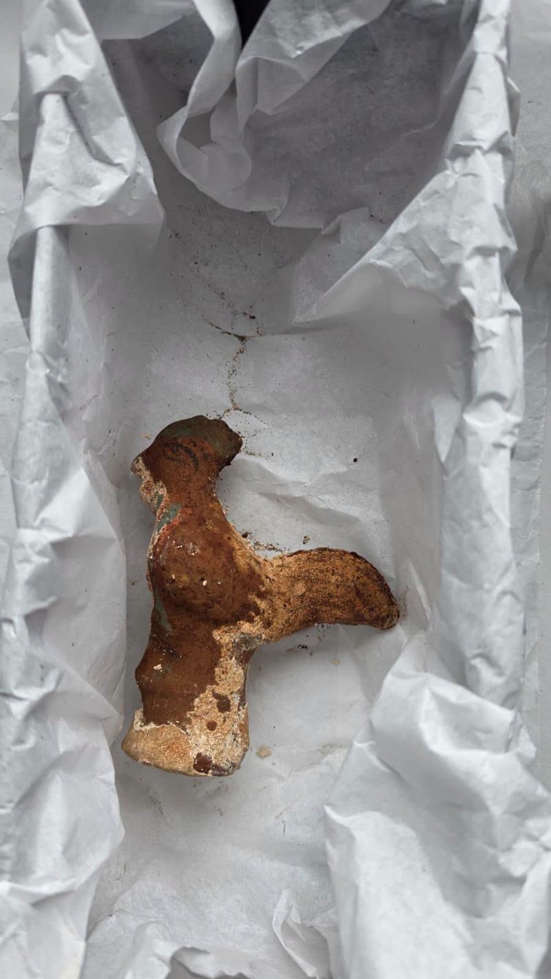 A small reddish brown clay rooster figurine lying on crumpled white tissue paper