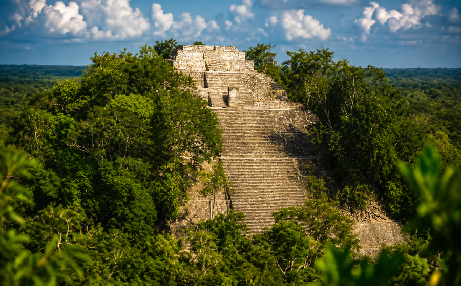 Aerial shot of Calakmul-style jungle ruins with visible structure. Calakmul pyramid rising above the jungle canopy in Campeche, Mexico.