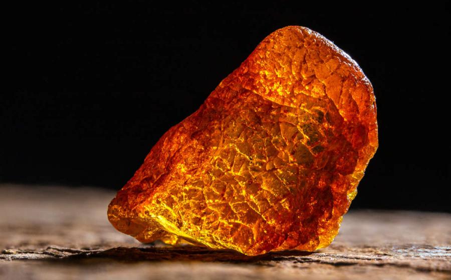 Natural amber. A piece of yellow transparent natural amber on large piece of dark stoned wood.
