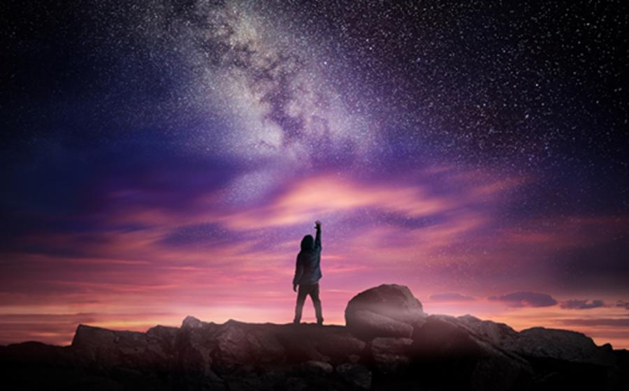 Man standing in a high place reaching up in wonder to the galaxy.