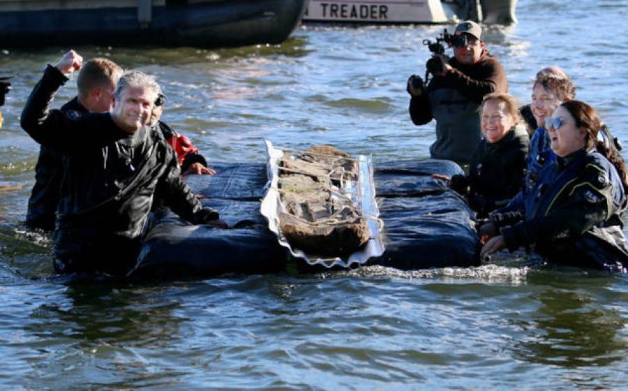 Volunteers and researhcers removing a 3,000 year old canoe from a lake.