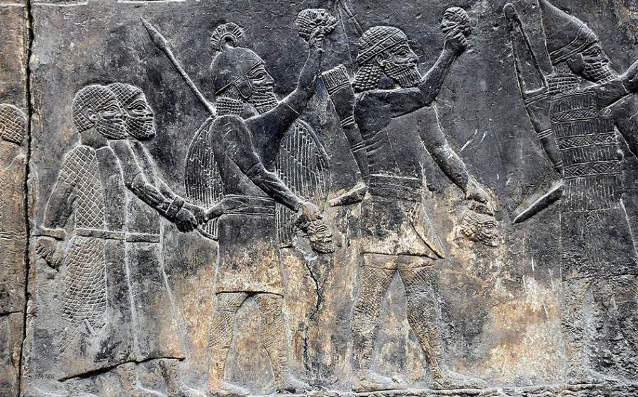 Assyrian soldiers carry beheaded heads of their prisoners as depicted on a wall in the South-West Palace at Nineveh, during the “First” Fall of Neneveh.          Source: Osama Shukir Muhammed Amin / CC BY-SA 4.0
