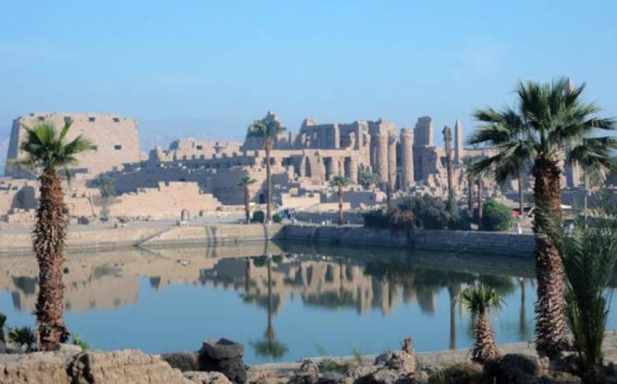 Karnak Temple Complex in Luxor, Egypt, showing the magnificent columns and sacred lake reflecting the ancient structures under clear blue skies.