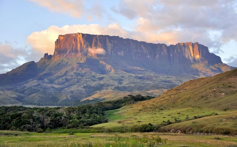 A beautiful, wide-angle shot of the neighboring Kukenan tepui at sunset, showing the massive, seemingly "cut" flat top and vertical walls glowing in golden light. Excellent representation of the tepui structure.