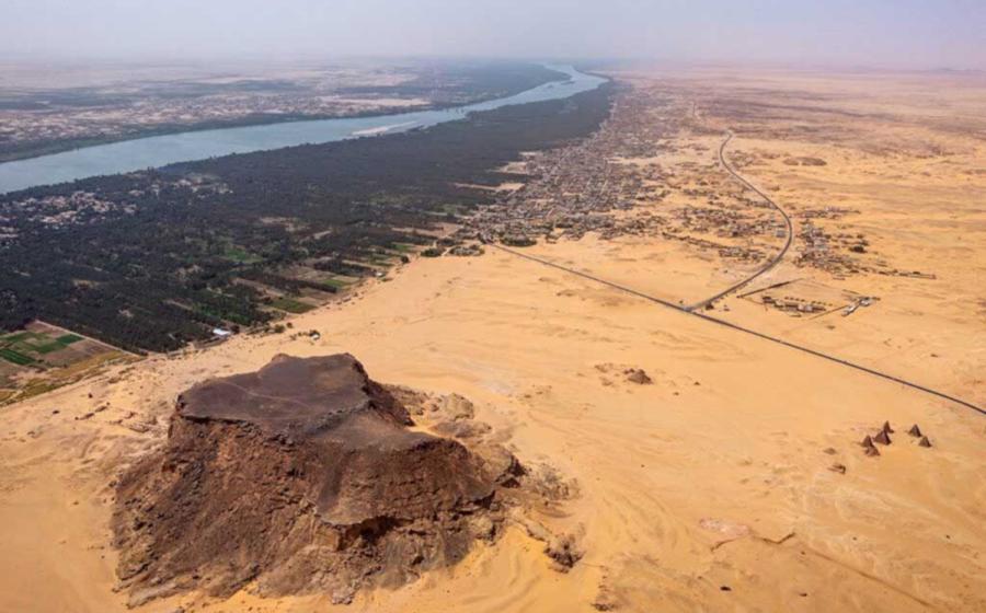 Jebel Barkal (ancient Napata), a UNESCO World Heritage site in northern Sudan, with the sandstone outcrop, temples, and pyramids in the foreground and the Nile and its floodplain in the background, viewed toward the southwest 