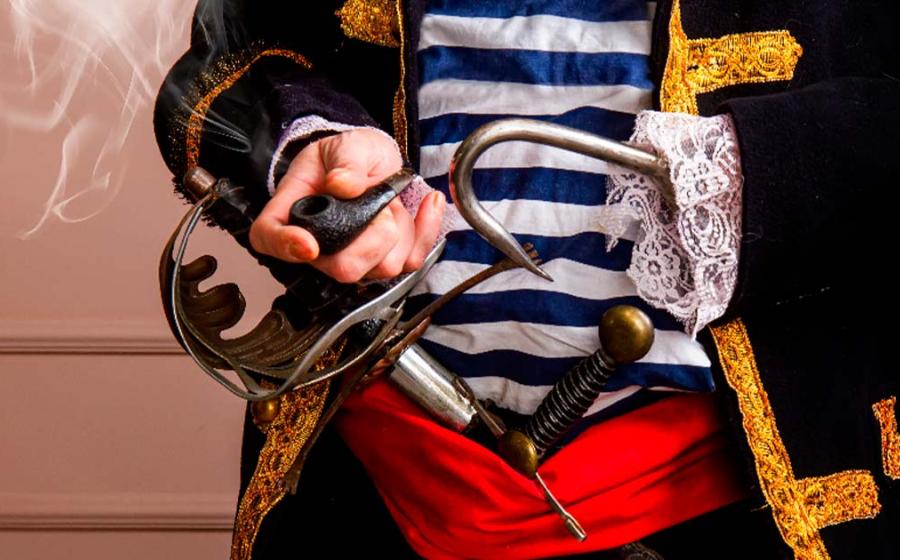 Close-up representation of an armed pirate captain in a frock coat and a vest with a sword, dagger and a hook, smoking a pipe. Source: sharpner/Adobe Stock