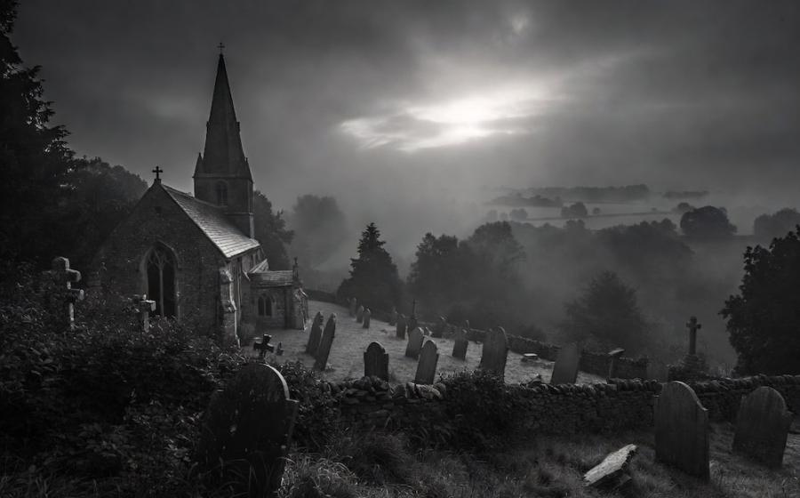 The ancient stone church of Pluckley stands dramatically in a foggy black-and-white landscape,