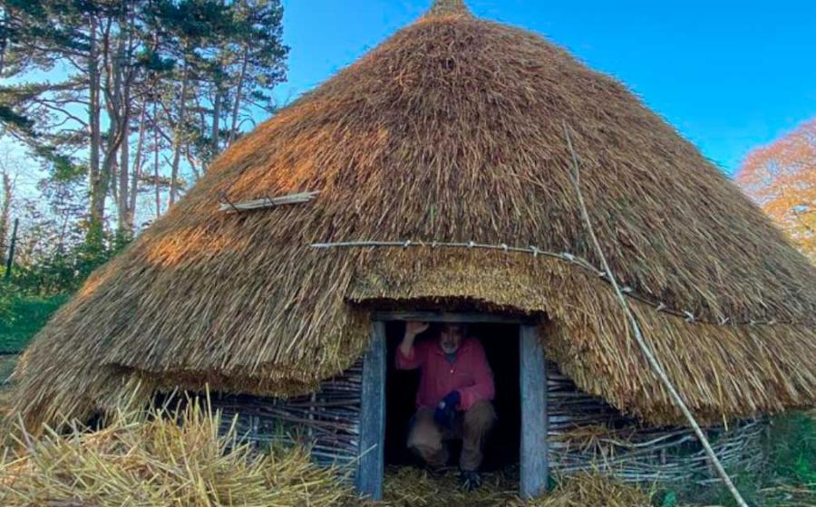 A second reconstructed roundhouse has been built by University of Dublin Centre for Experimental Archaeology students, after the first was subject to arson. Dr. Aidan O’Sullivan, crouched in the entryway of the roundhouse his students built. Source: UCD Centre for Experimental Archaeology