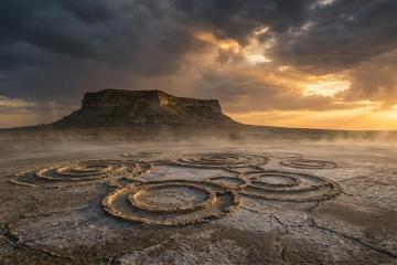 A haunting plateau rises over the cracked, salt-crusted desert. Mysterious circles etched into the ground hint at ancient secrets. Dramatic light and low mist shroud the landscape in enigma.