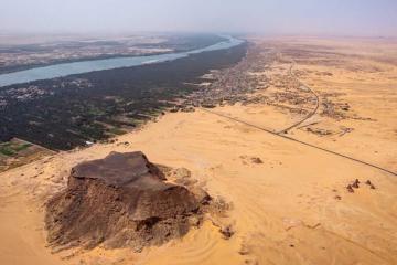 Jebel Barkal (ancient Napata), a UNESCO World Heritage site in northern Sudan, with the sandstone outcrop, temples, and pyramids in the foreground and the Nile and its floodplain in the background, viewed toward the southwest 