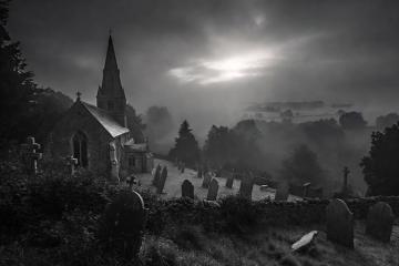 The ancient stone church of Pluckley stands dramatically in a foggy black-and-white landscape,