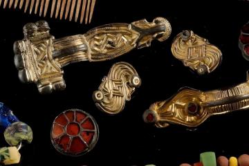 Grave items from Szeleste are the center of a shield, or umbo (upper right), various brooches (center), mosaic beads, and an antler comb (top left).