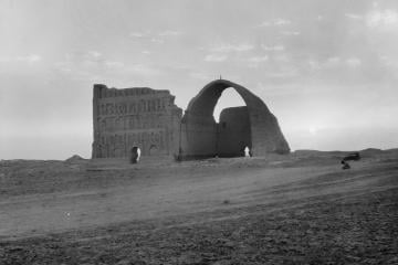 Black and white photo of the great brick arch of Ctesiphon standing in flat desert at sunset