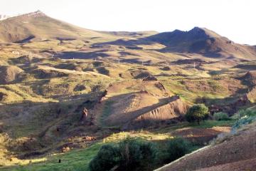 Grassy hillside valley in eastern Turkey with a long, raised, boat-shaped earth formation in the center and mountains behind