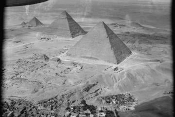 Black and white aerial photograph of the three Giza pyramids in a diagonal line above a village