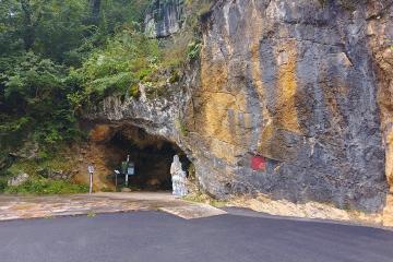 The rock face and arched entrance of the Isturitz and Oxocelhaya caves, with a paved road in front and trees above