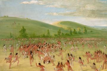 Hundreds of Choctaw players holding sticks chase a ball across a wide green field below rolling hills