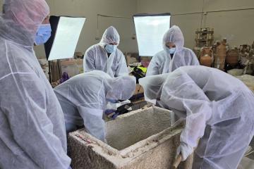 Museum specialists in white protective suits leaning over an open stone sarcophagus