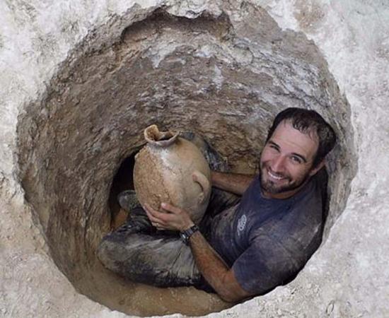 David Tanami, an Israel Antiquities Authority archaeologist, works his way into the narrow tomb opening to bring out a jar at a Canaanite burial site near Jerusalem's Biblical Zoo.