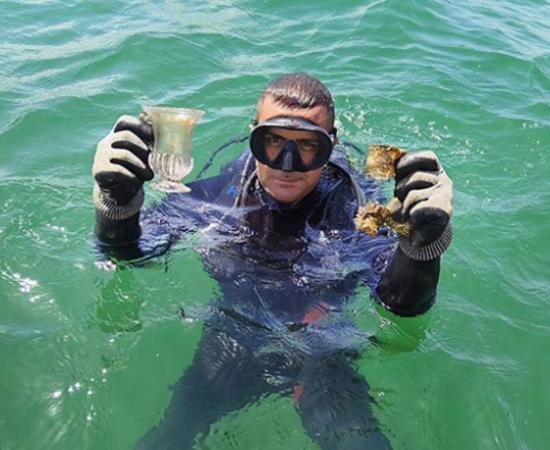 A marine archaeologist holds up intact glass vessels.	Source: Regional Historic Museum Burgas