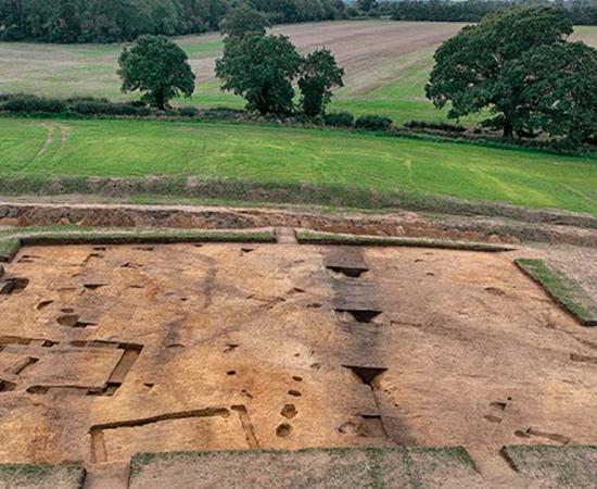 Arial photograph of the excavations at Rendlesham in 2023, showing the archaeological remains, including the probable temple or cult house (left hand side) and boundary ditch (center). Source: © Suffolk County Council; photo by Jim Pullen