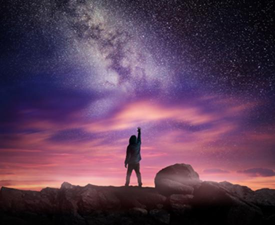 Man standing in a high place reaching up in wonder to the galaxy.