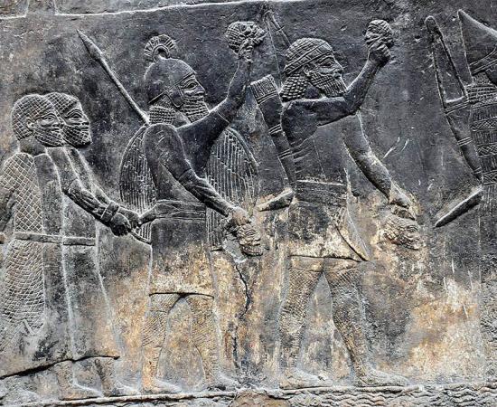 Assyrian soldiers carry beheaded heads of their prisoners as depicted on a wall in the South-West Palace at Nineveh, during the “First” Fall of Neneveh.          Source: Osama Shukir Muhammed Amin / CC BY-SA 4.0