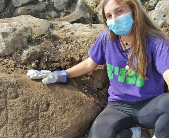 The image shows Ofri Eitan of the Kfar Hanasi pre-military Academi next to a large engraved stone discovered at the Golan Heights fort.             Source: Tidhar Moav / Israel Antiquities Authority