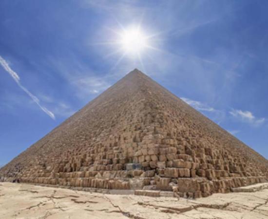 The Pyramid of Cheops illuminated by the sun in backlight, with people entering inside to visit it. The area with the great pyramids of Giza, Egypt. Source: Alfredo /Adobe Stock