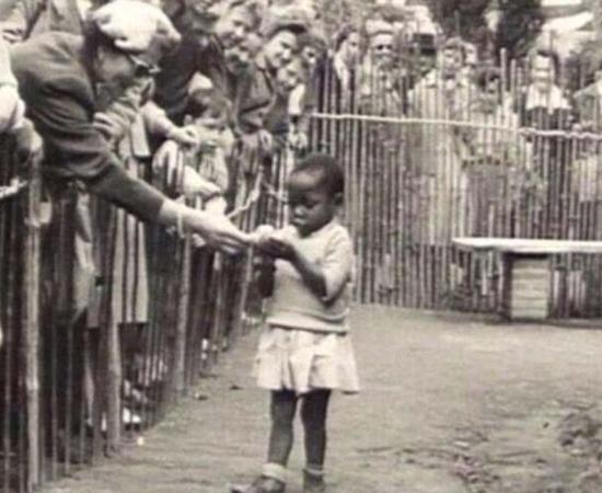 An African girl is shown at the 1958 Expo in Brussels, Belgium that featured a 'Congo Village' with visitors watching her from behind wooden fences