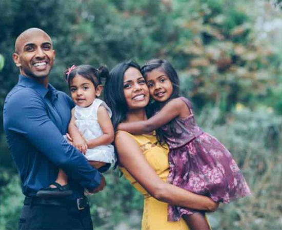 Indian family standing and smiling holding their kids in the park. Source: kristineldridge/Adobe Stock