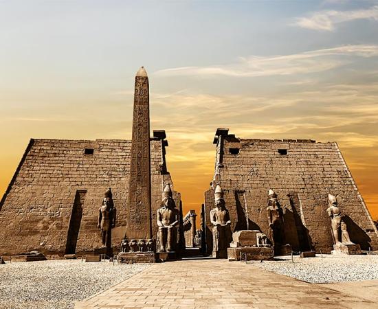 Entrance to the Luxor Temple at sunset showing the obelisk and statues of pharaohs