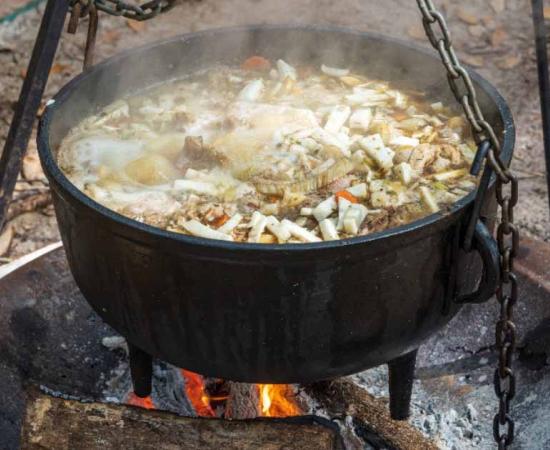 A meat and vegetable stew in a black cauldron cooking over an open fire. Source: Sunshower Shots/Adobe Stock