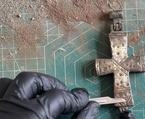 A conservator applies delicate conservation work to the intact, permanently sealed bronze reliquary cross found at Lystra.