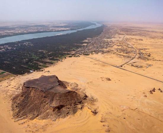 Jebel Barkal (ancient Napata), a UNESCO World Heritage site in northern Sudan, with the sandstone outcrop, temples, and pyramids in the foreground and the Nile and its floodplain in the background, viewed toward the southwest 