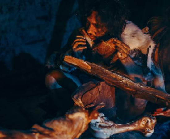 Neanderthal cannibals eating a meat feast by a fire.