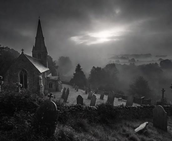 The ancient stone church of Pluckley stands dramatically in a foggy black-and-white landscape,