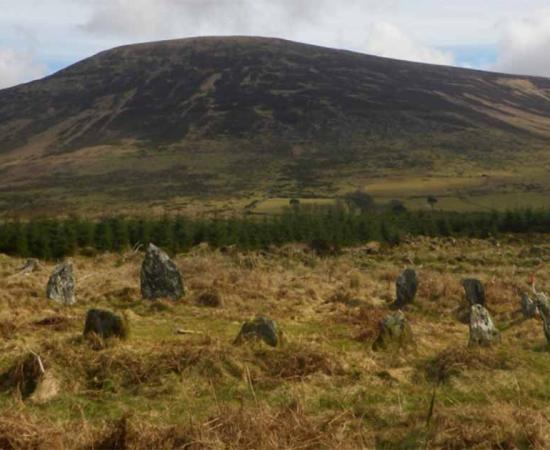 Prehistoric Irish monuments of Late Bronze Age stone circle at Boleycarrigeen, with Keadeen cursus near the summit of the mountain in the background        Source: J. O’Driscoll/Antiquity